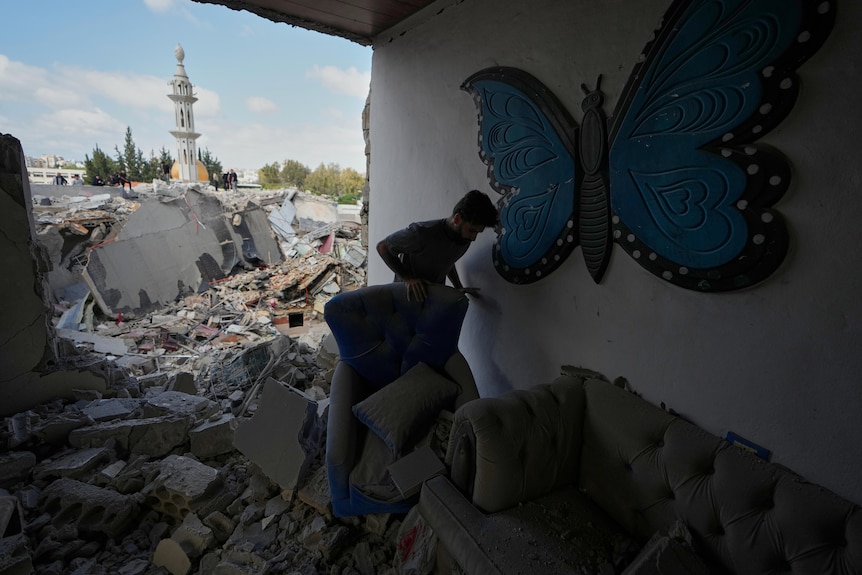 A young, dark-haired man amid the rubble of a building destroyed in a military attack.