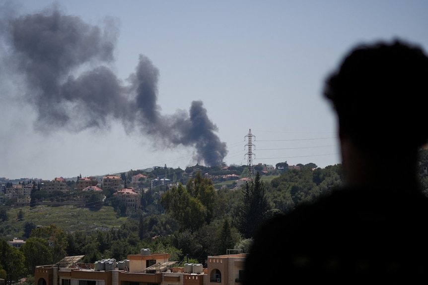 The silhouette of a man looks into the distance at black smoke billowing into the sky.