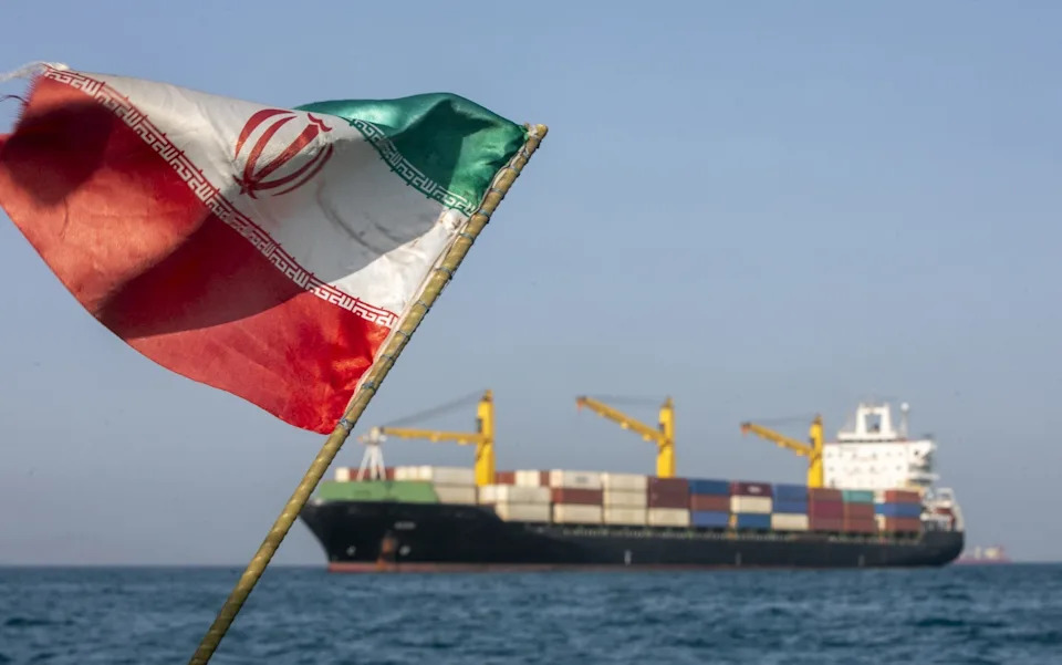 An Iranian flag fluttering with the Strait of Hormuz in the background