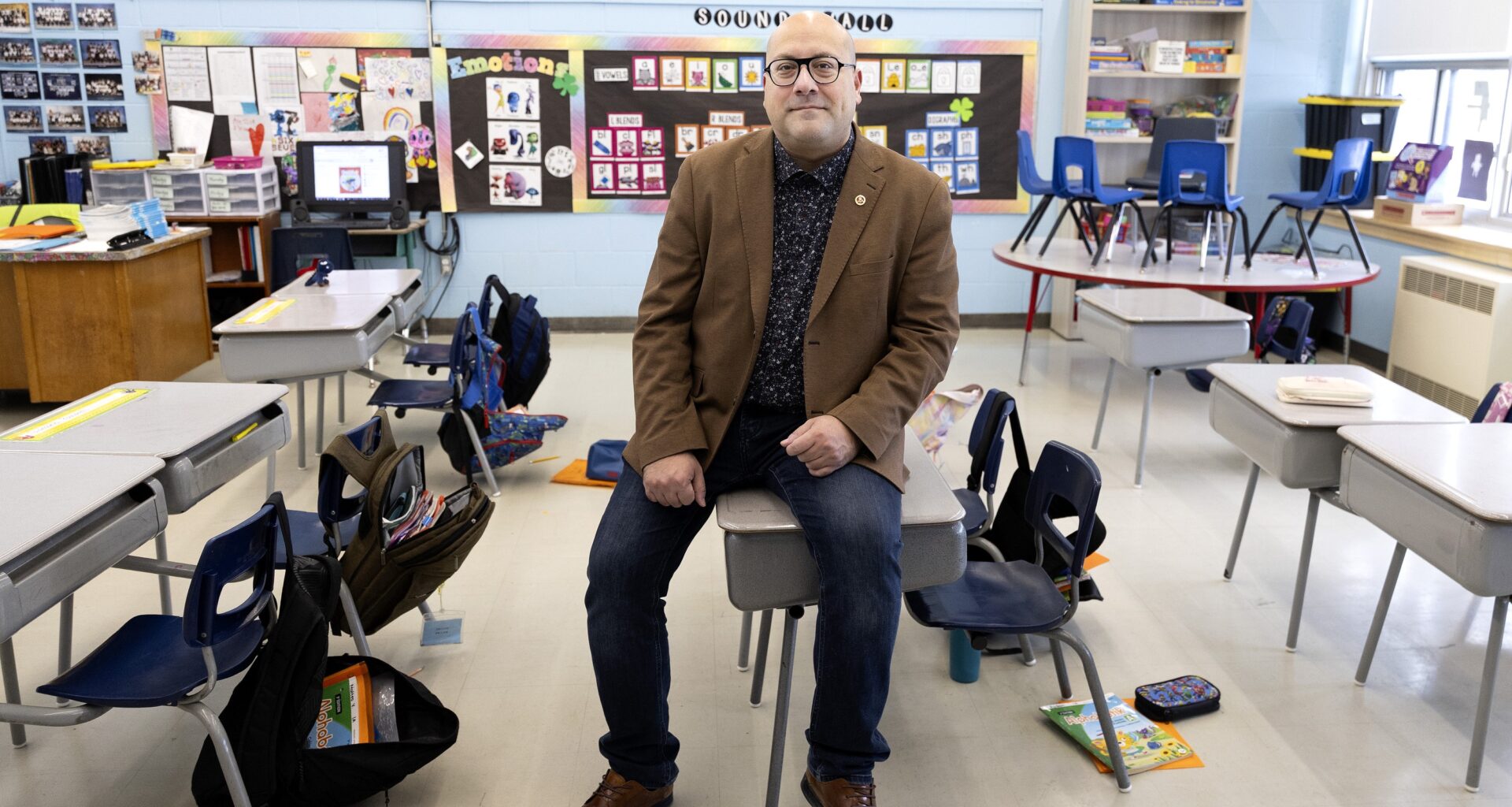 English Montreal School Board chair Joe Ortona sits on a small desk in an elementary school classroom.