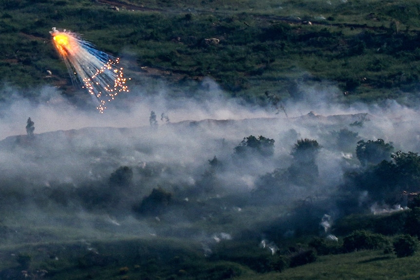 An explosion is seen in the air, surrounded by white smoke that hovered over a green field