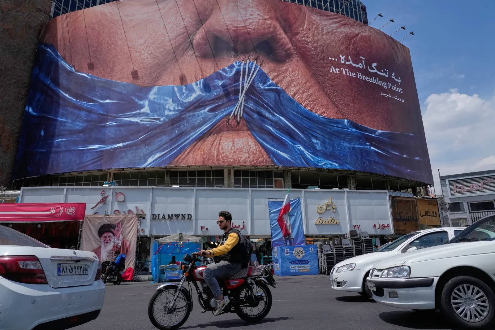 Vehicles drive past a billboard with a graphic showing the Strait of Hormuz and sewn lips of U.S. President Donald Trump in a square in downtown Tehran, Iran, on May 2. (AP Photo/Vahid Salemi)