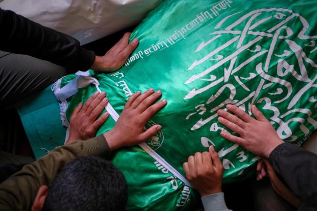 Palestinians place their hands on the body of Izz al-Din al-Haddad.
