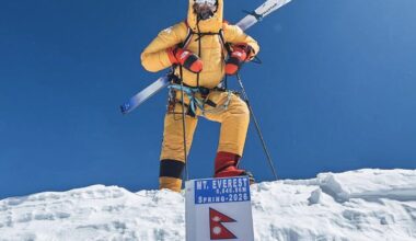 Bartek Ziemski stands on the summit of everest with skis strapped to his bckpack and an air-trimming mask.