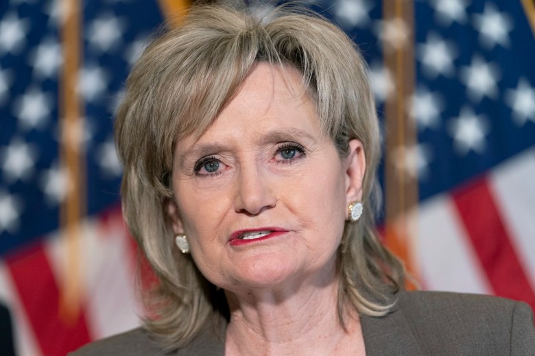 A closeup of Cindy Hyde-Smith speaking in front of a wall of flags
