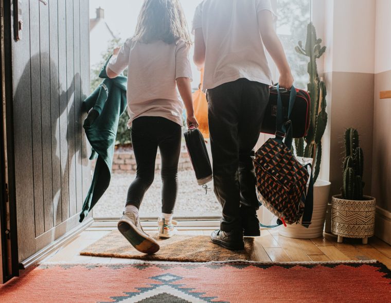Two young children wearing school uniforms exit their front door - stock photo