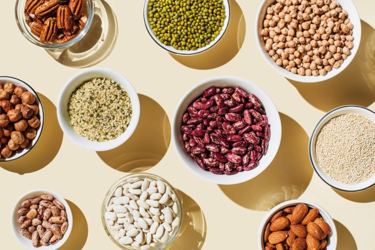 Various kinds of vegan protein sources on beige background. Set of food supplements. Gluten free cereals as ground hemp seeds, quinoa. Nuts and legumes (green mung beans, chick-pea, red lentil, kidney bean, almonds, hazelnuts). Flat lay, top view - stock photo