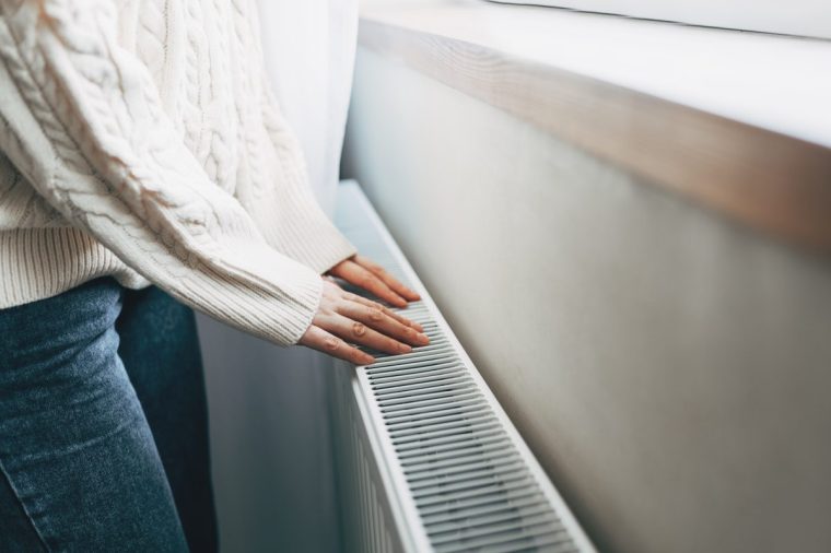 Central heating problem at home. Woman checking heating radiator in cold apartment - stock photo