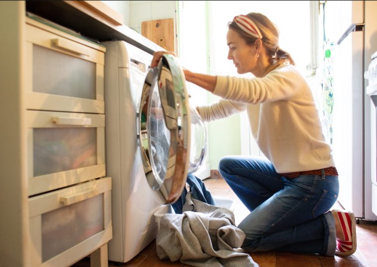 Woman loading washing machine in the kitchen - stock photo