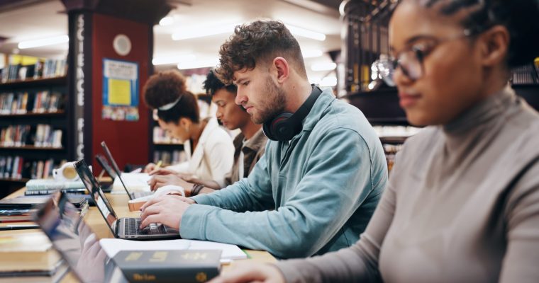 Education, laptop and typing with student friends in library of university together for learning or study. Computer, development or growth with serious men and women on college campus for scholarship - stock photo