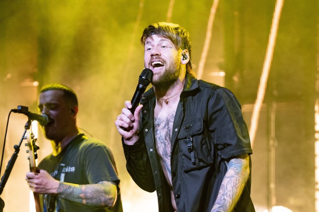 Caleb Shomo performs onstage in a black open t-shirt.