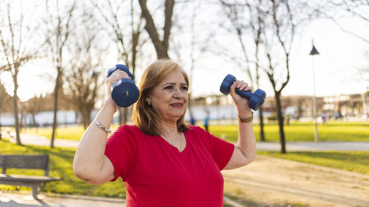Mature woman exercising with dumbbells in park at sunset - stock photo