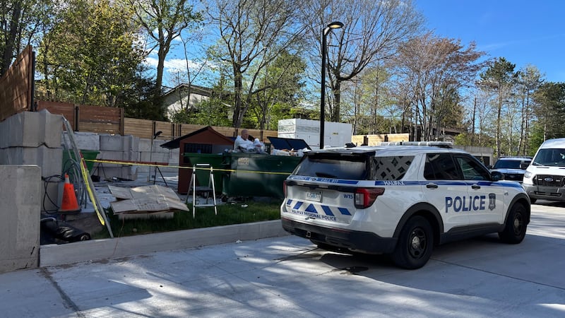 A police car in pictured next to a dumpster with police tape.