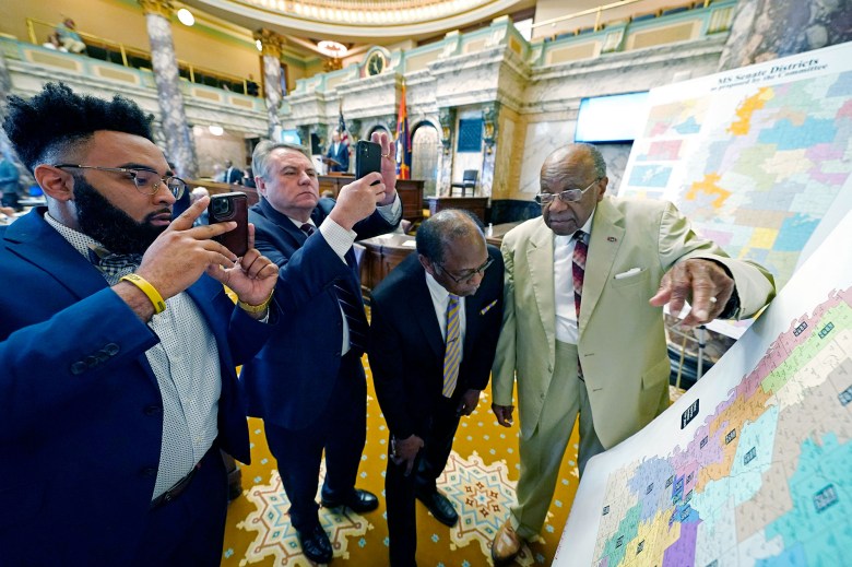 Four men look at and take pictures of maps showing MS Senate Districts