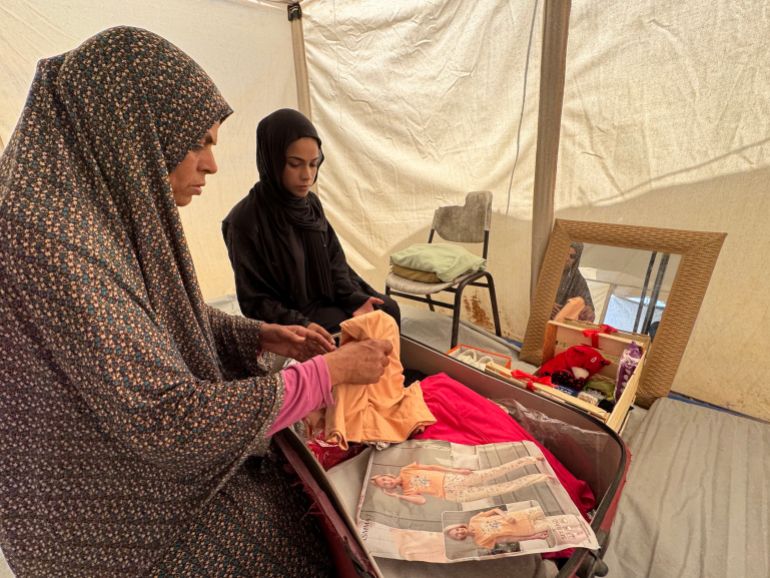 Saja and her mother, Samira, try to arrange her few belongings inside the tent, with the absence of a wooden wardrobe to store them [ Al Jazeera]