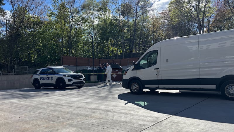 A police car in pictured next to a dumpster with police tape.