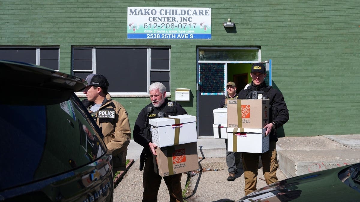 Federal agents carry boxes out of a green building