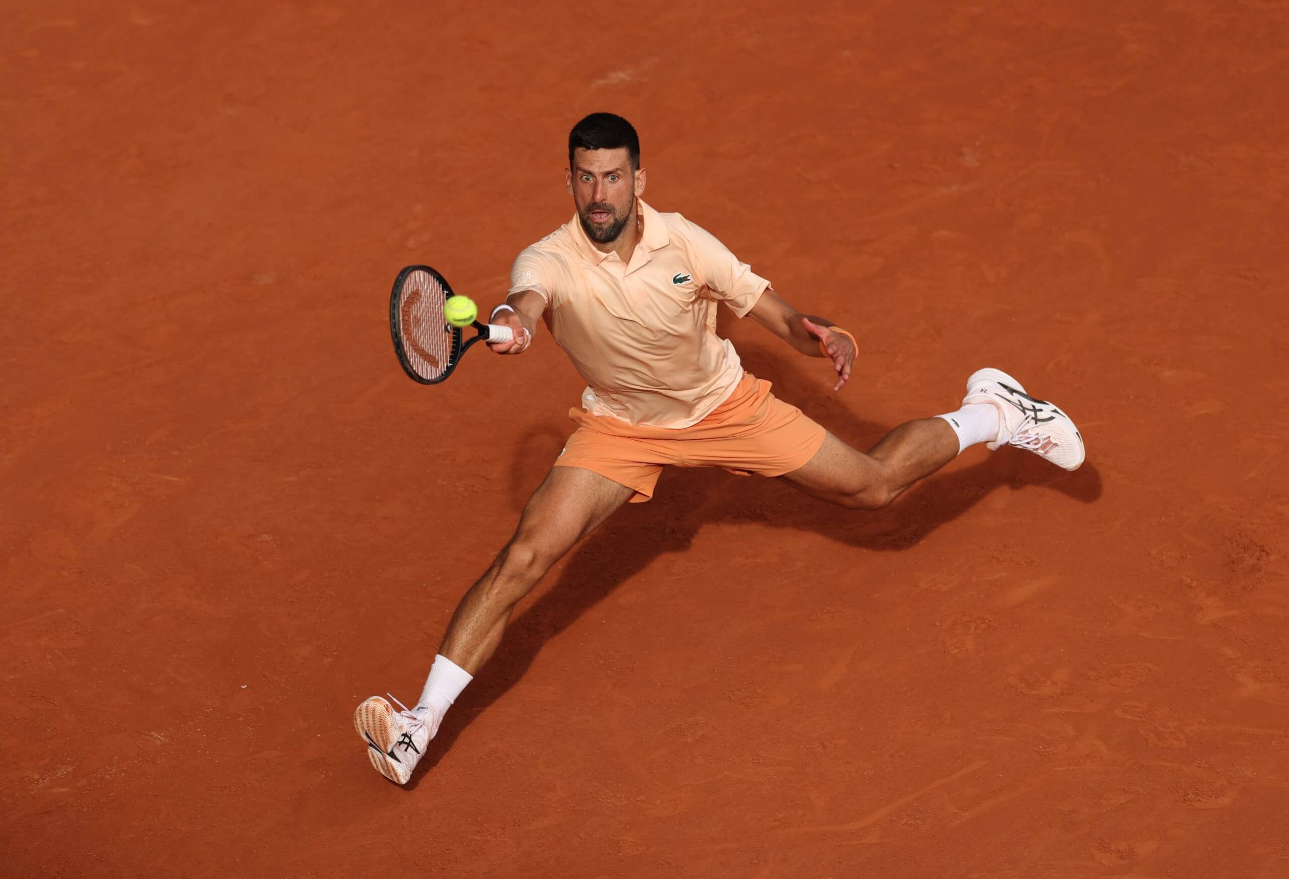 Novak Djokovic stretches out to hit a forehand on the run on a clay tennis court