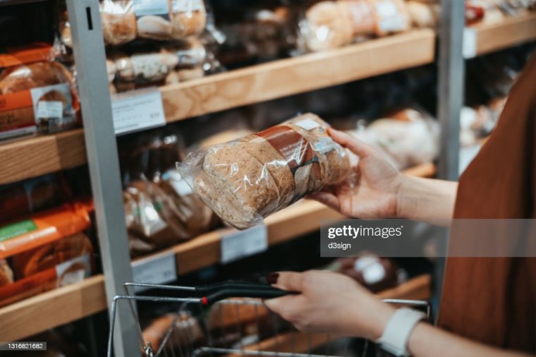 Young Asian woman carrying a shopping basket grocery shopping in a supermarket, shopping for packaged fresh wholegrain bread in the bread aisle. Healthy eating lifestyle