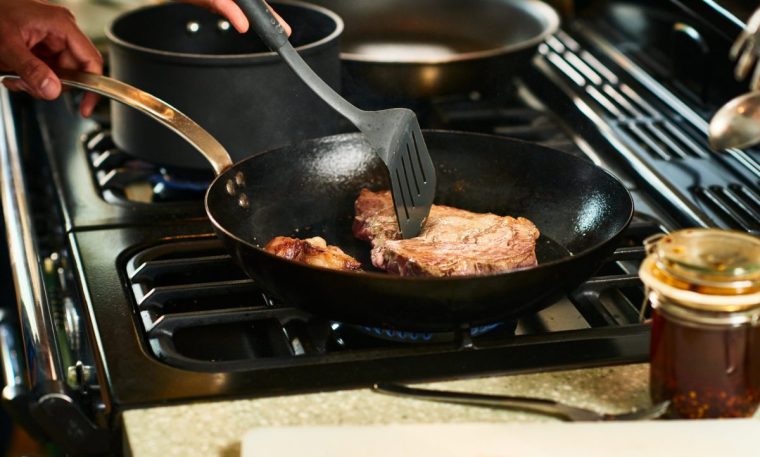 Person cooking on kitchen hob turning steak with a spatula