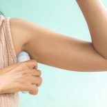 Woman applying deodorant roll on under armpit