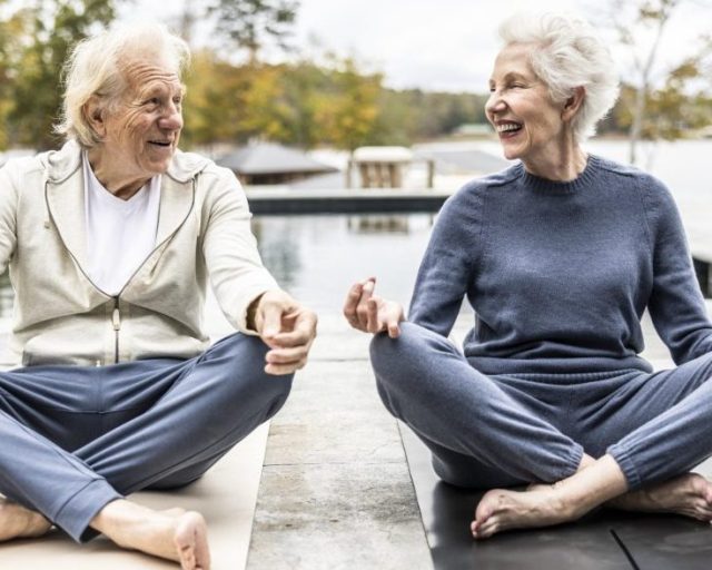 Senior couple practicing yoga in front of beautiful pool overlooking lake