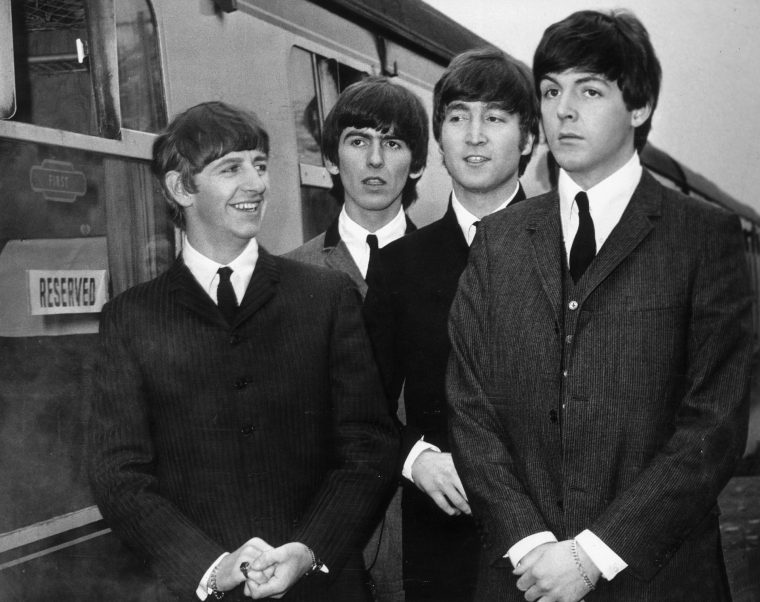 British rock group The Beatles stand next to a train on a station platform in Richard Lester's film 'A Hard Day's Night', 1964. Left to right, Ringo Starr, George Harrison, John Lennon (1940 - 1980) and Paul McCartney. (Photo by United Artists/Archive Photos/Getty Images)