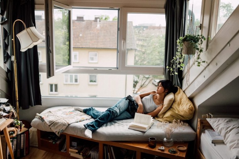 A serene moment of relaxation, with a person reclining by a window while reading in a comfortable, warmly-lit room adorned with decorative details.