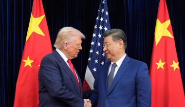 President Donald Trump and Chinese President Xi Jinping shake hands between both nations' flags.