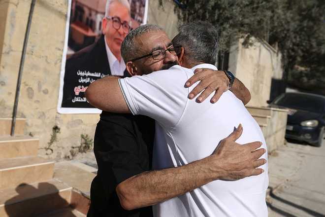 PALESTINIAN-ISRAEL-CONFLICT-MEDIA-PRISONER Palestinian journalist Ali al-Samoudi is hugged by a relative as he stands in front of a large image of himself taken before he was detained by the Israeli army and held for a year, at his home in the northern city of Jenin, in the Israeli-occupied Palestinian West Bank on May 1, 2026. Sixty-year-old Al-Samoudi was released following one-year in detention in the Israeli Naqab Prison, located in southern Israel. He was released and checked at the Jenin Hospital where he said, "I was 120 kilogrammes; my weight now is barely 60 kilogrammes". Israel has jailed an increasing number of journalists since 2023, the year of Hamas's unprecedented October 7 attack on Israel, which responded with a devastating war in the Gaza Strip. (Photo by JAAFAR ASHTIYEH / AFP via Getty Images)