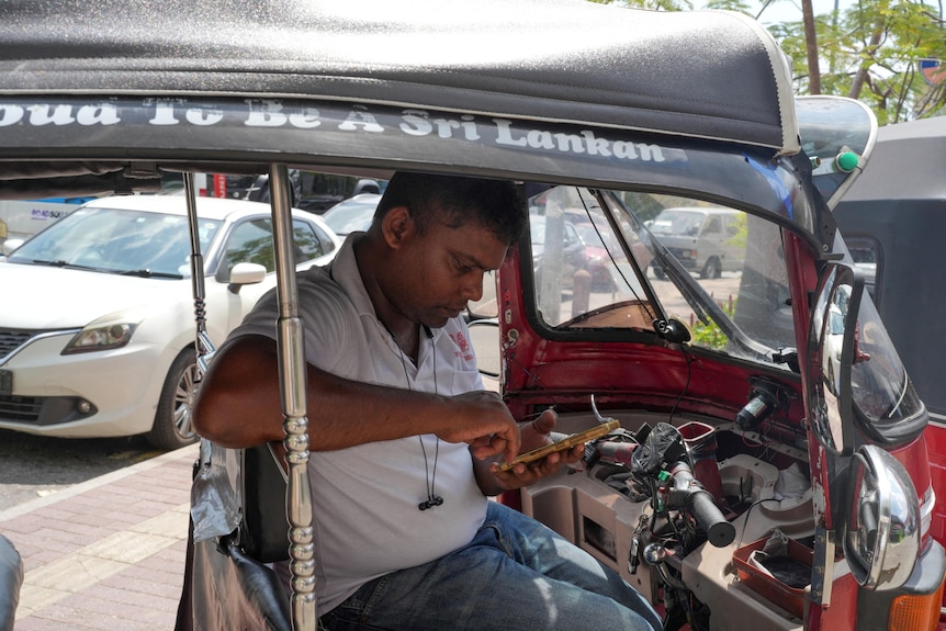 a man sits inside a rickshaw outside a fuel station 