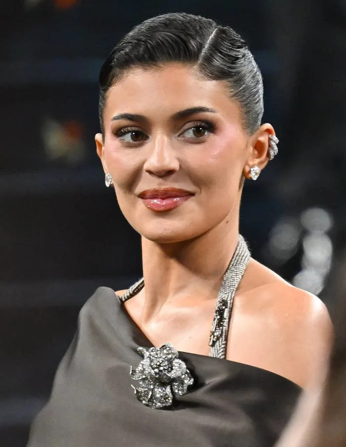 Kylie Jenner in elegant off-shoulder dress with floral brooch, styled hair, and statement earrings at a formal event