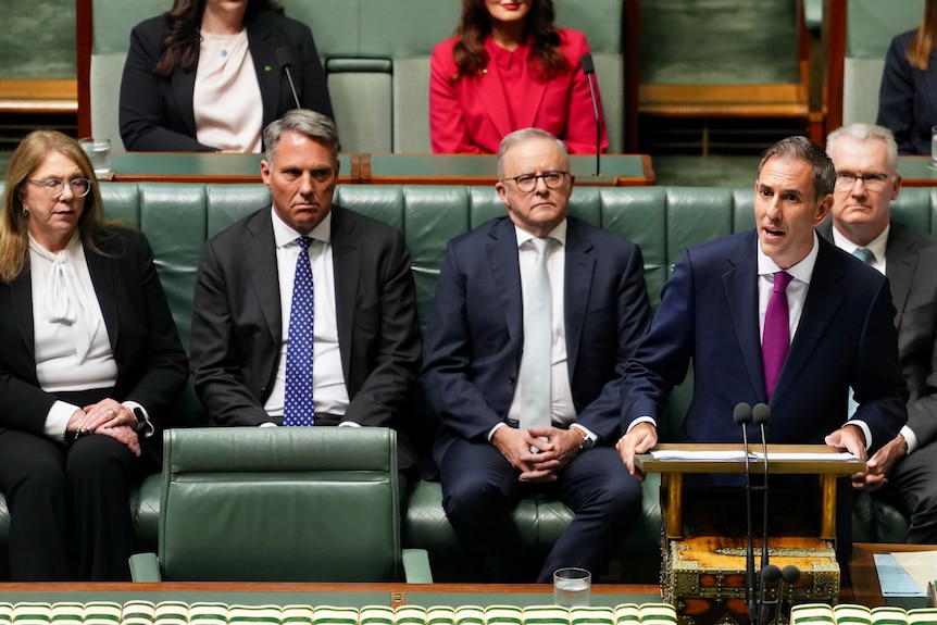 Jim Chalmers stands and speaks in the House of Representatives as Anthony Albanese sits behind him.