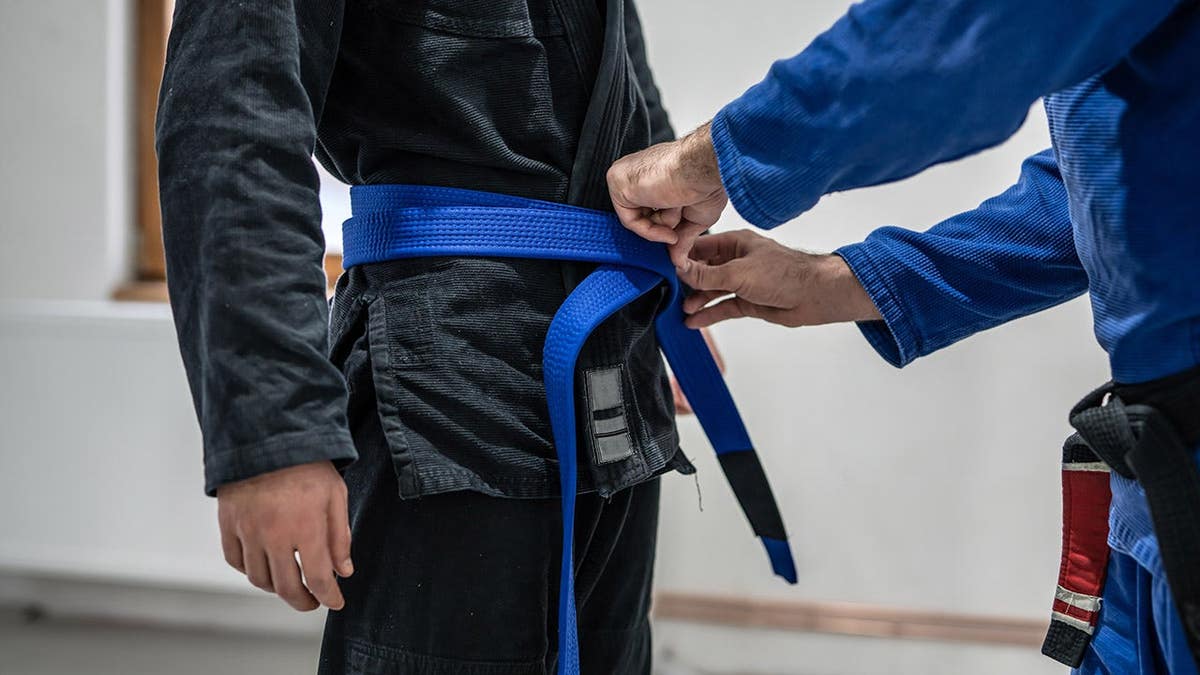 Black belt instructor tying blue belt on student's waist during Brazilian Jiu Jitsu promotion.