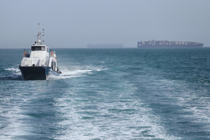 a patrol boat in the water with some cargo ships in the distance