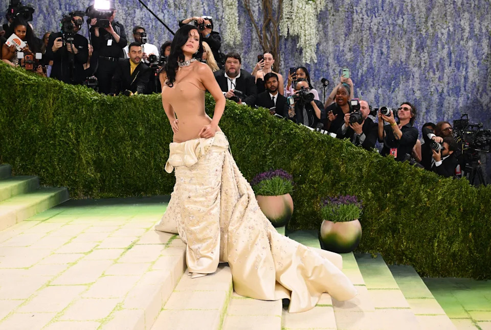 Kylie Jenner in elegant gown posing confidently on stairs at a high-profile event, surrounded by photographers and lush greenery