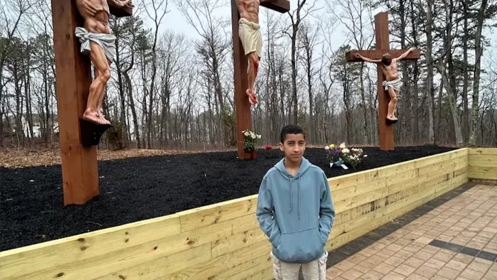 Cesar Albarracin Guncay standing in front of three crucifixes in a wooded area.