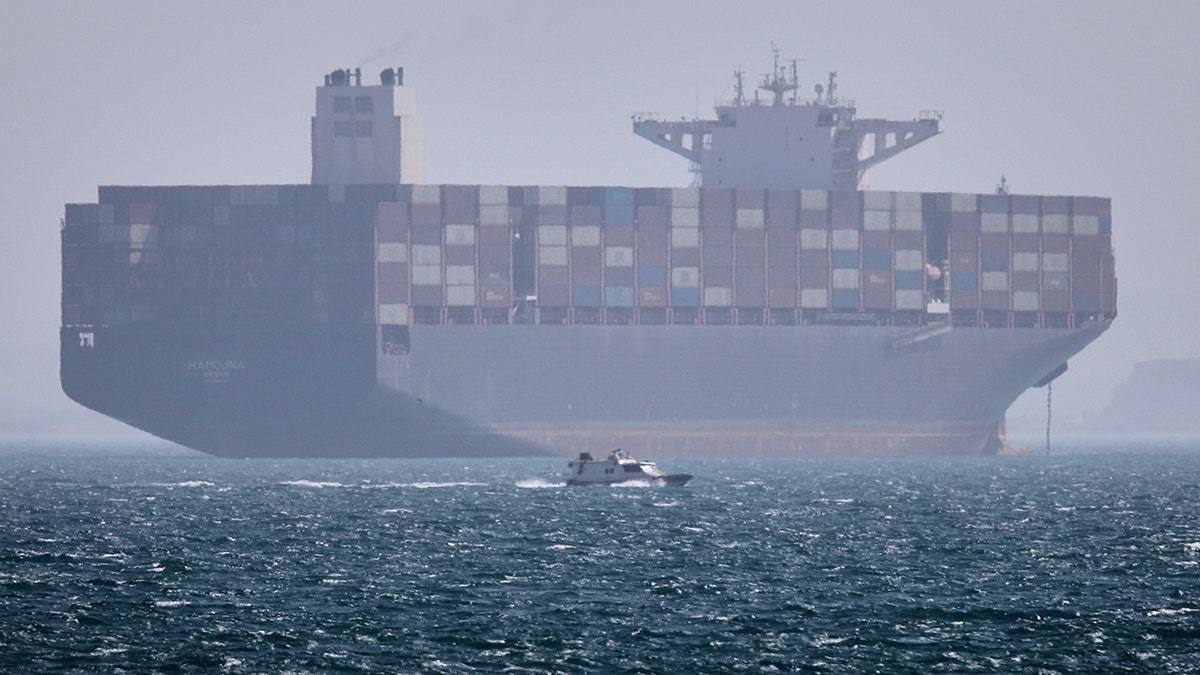A container ship sitting at anchor in the Strait of Hormuz as a motorboat passes in the foreground.