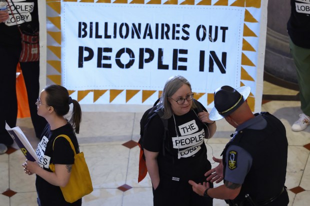 A demonstrator talks with a police officer as fellow demonstrators hold banners about stopping corporate tax breaks and using tax revenue to fund communities and education during the spring legislative session at the State Capitol, May 30, 2026, in Springfield. (John J. Kim/Chicago Tribune)