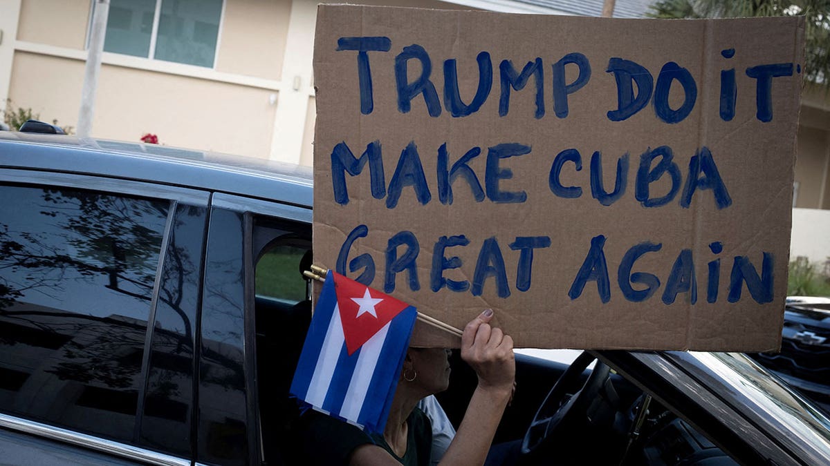 A woman holding a sign and Cuban flags at a protest in Miami, Florida