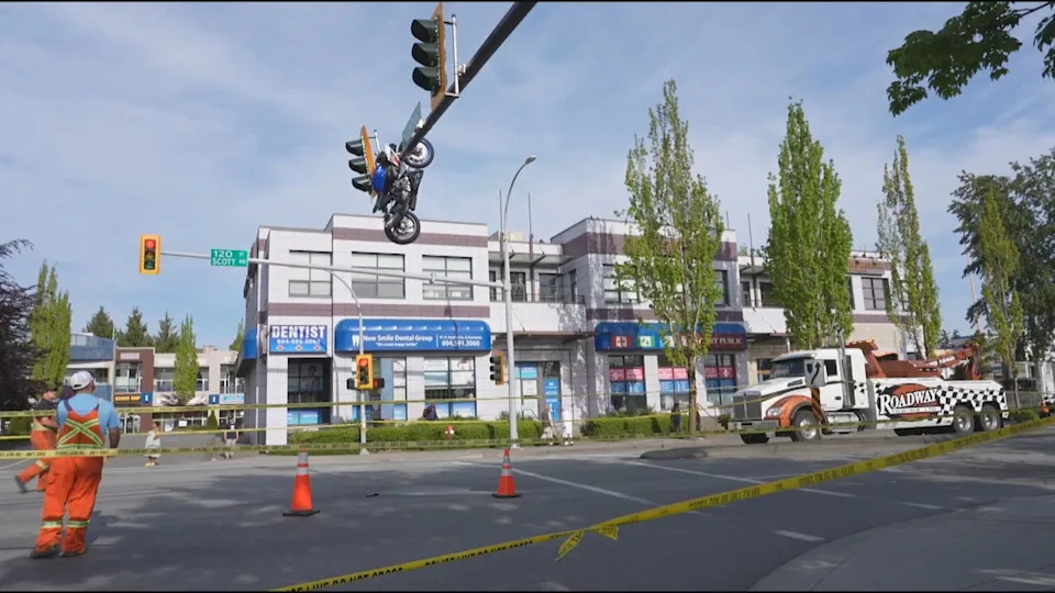Crews work to remove the motorcycle dangling from an overhead traffic signal on Saturday.
