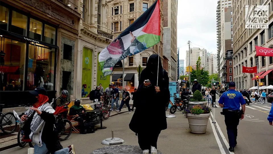 Demonstrator carrying Abu Obaida imagery walks through Manhattan during an anti-Israel protest.