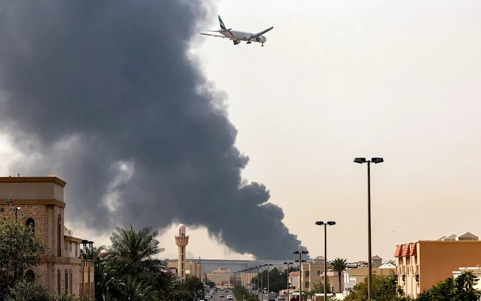 An Emirates aircraft prepares for landing as a smoke plume rises from an ongoing fire near Dubai International Airport in Dubai