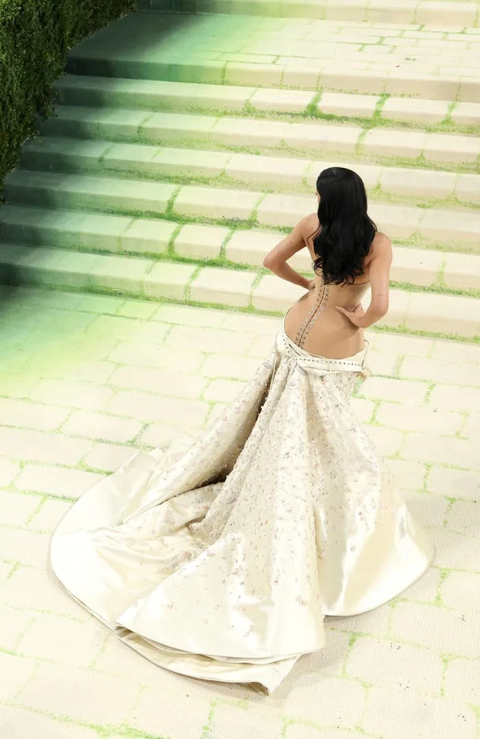 Kylie Jenner in a strapless gown with a back cutout, posing on decorative steps. Elegant and dramatic attire