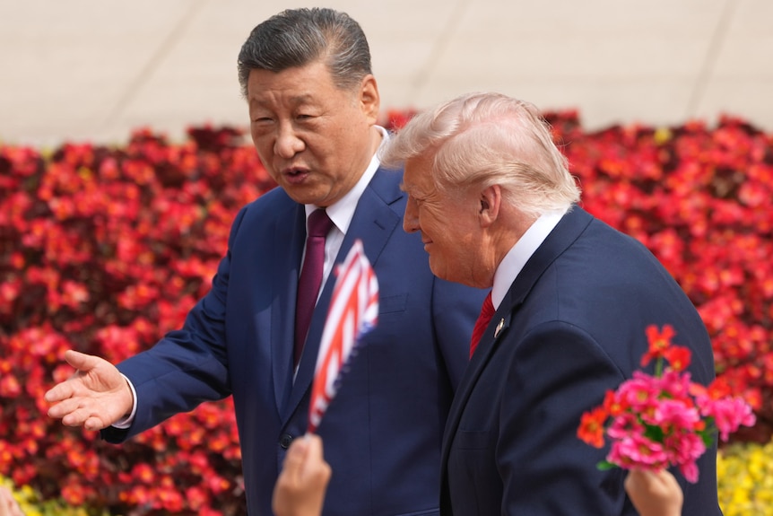 President Donald Trump walks at a welcome ceremony with China's President Xi Jinping in front of red flowers.