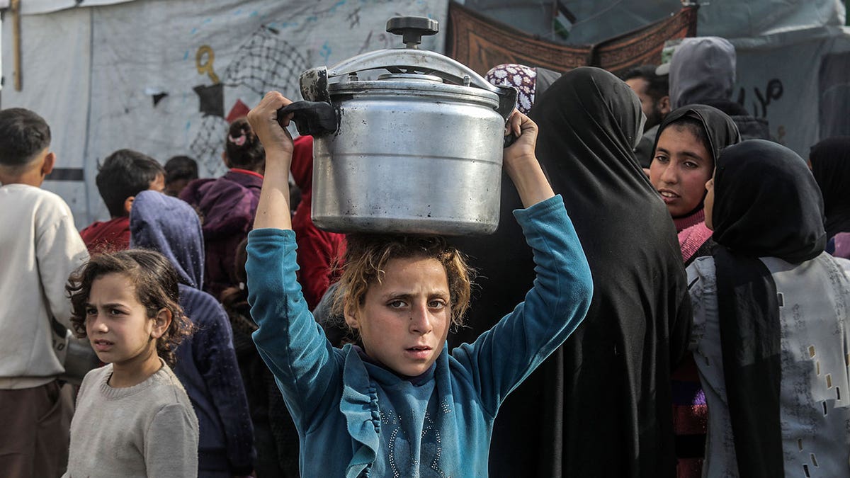 Displaced Palestinians, including children, wait in line to receive hot meals in Khan Yunis, Gaza