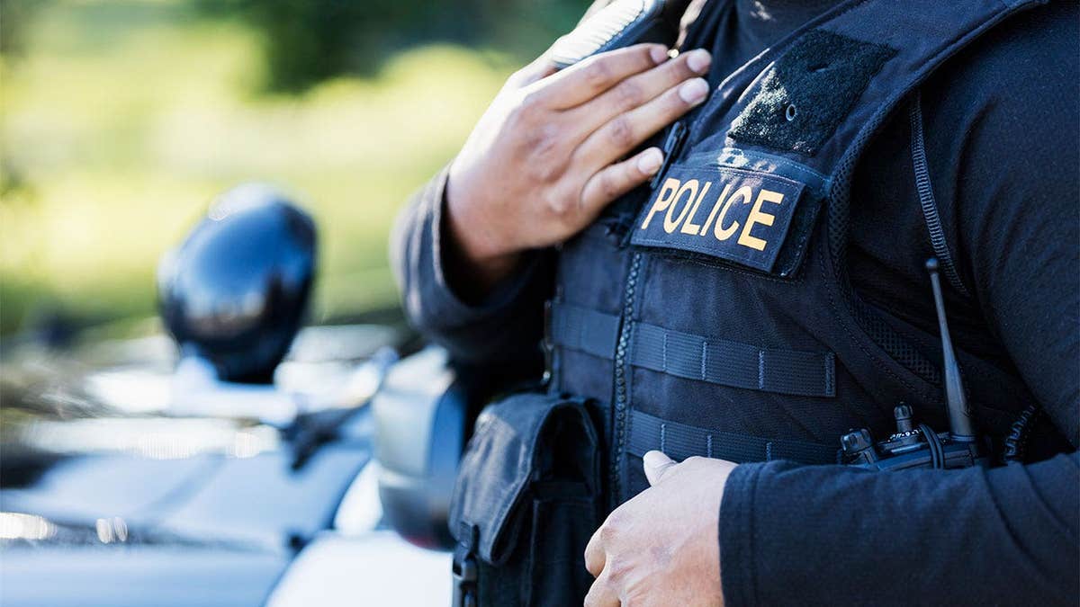 Cropped view of a police officer standing outside patrol car