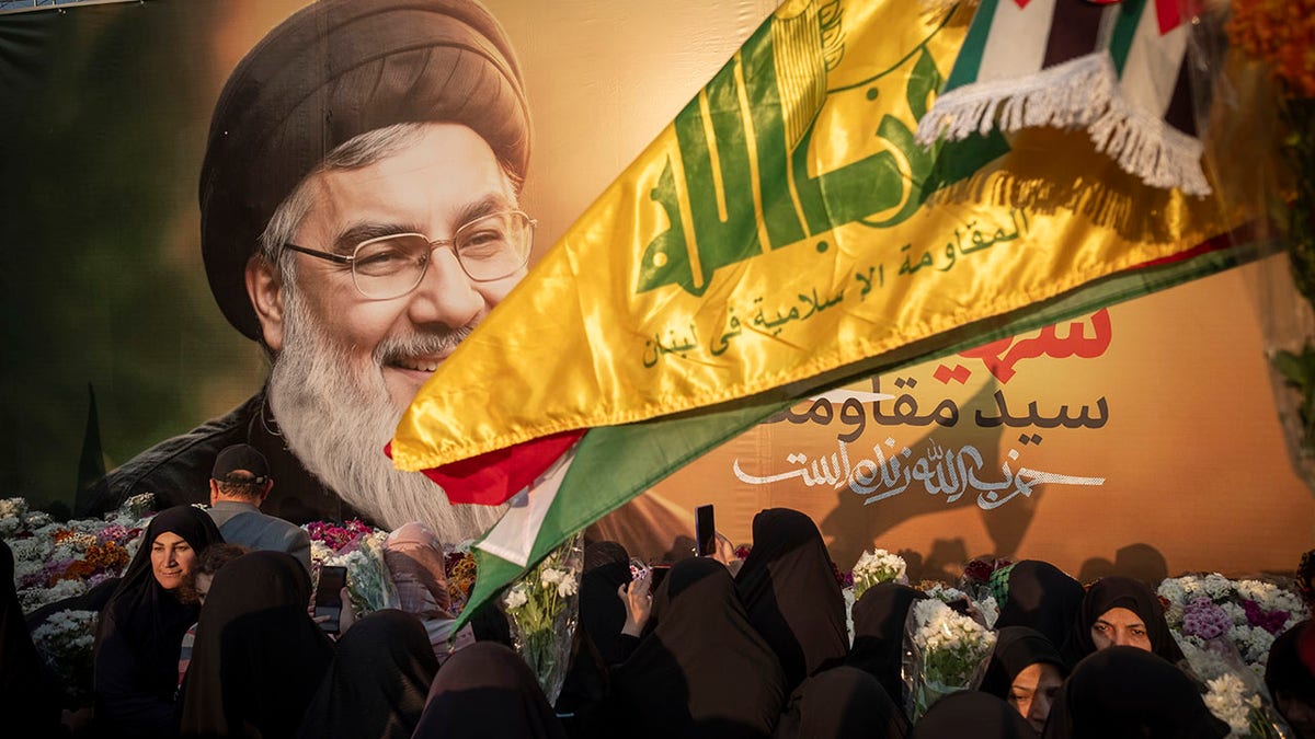 Iranian protesters carrying flowers in front of a large banner of Hassan Nasrallah in Tehran