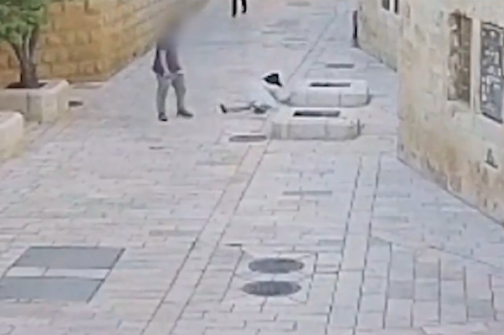 A blurry, high-angle image shows a person lying on the ground in a paved alley, with another person standing nearby.