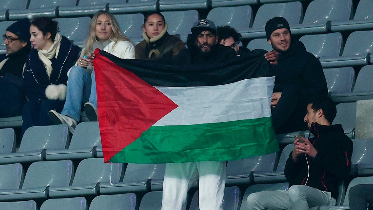 A fan holding a Palestine flag at an Israel-France soccer match